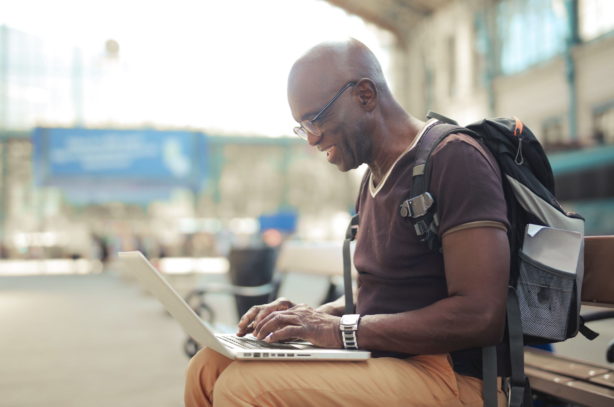 A male African digital nomad sitting on a bench and working remotely on his computer 