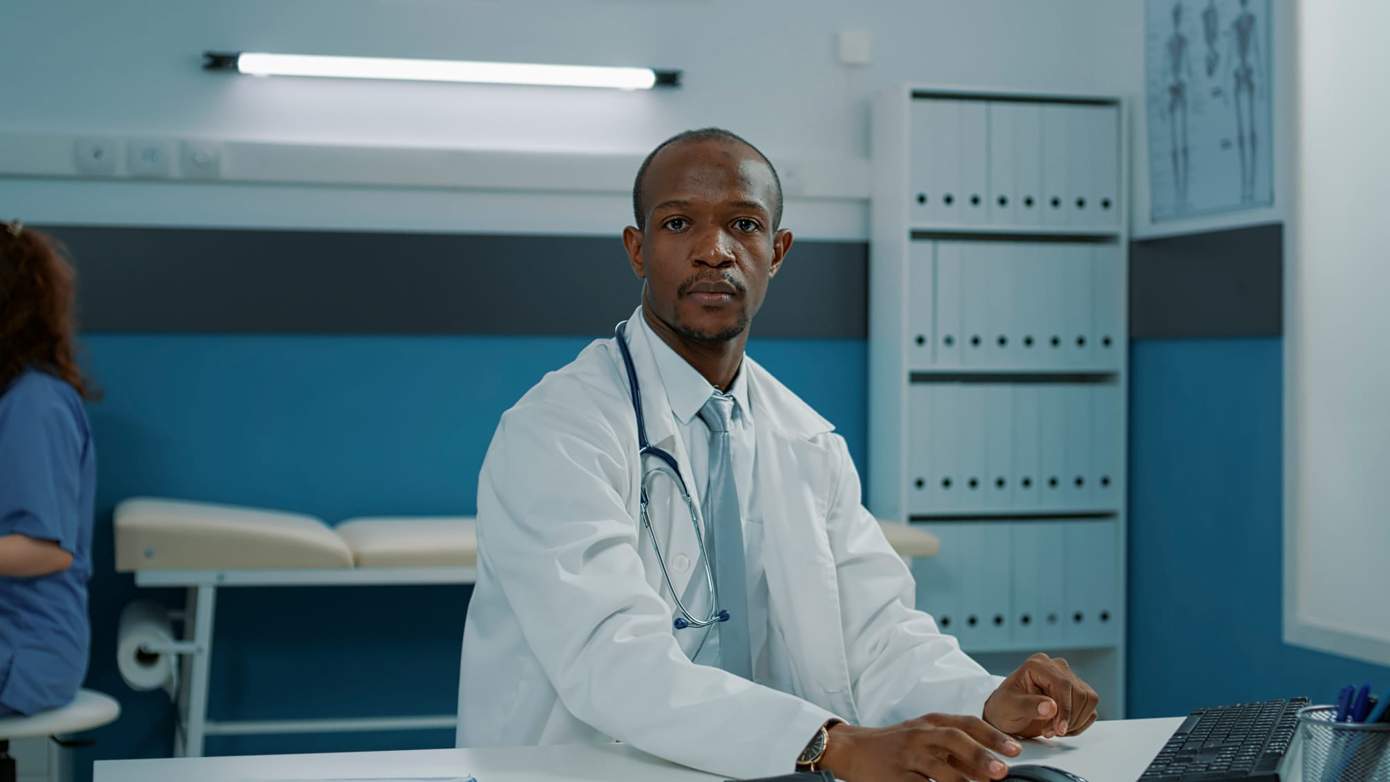 Doctor using computer in cabinet, working on health support. General practitioner wearing white coat and stethoscope